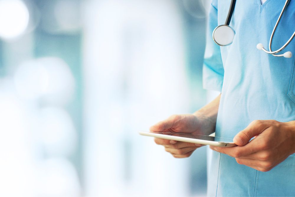 A doctor holding and looking into a tablet.